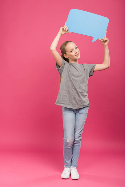 smiling preteen kid holding blue speech bubble, isolated on pink - Photo, image