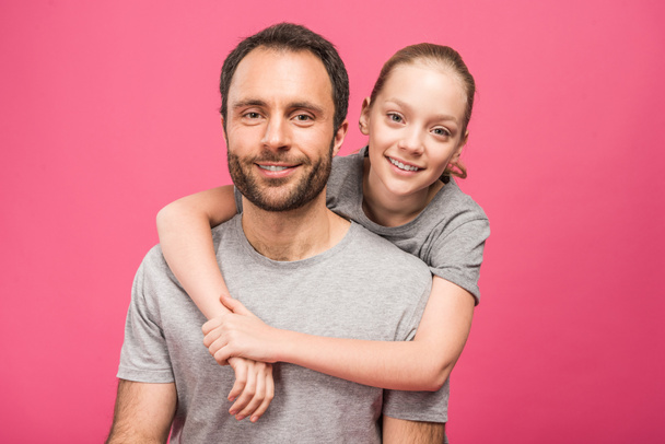 smiling blonde daughter hugging her father, isolated on pink - Фото, изображение