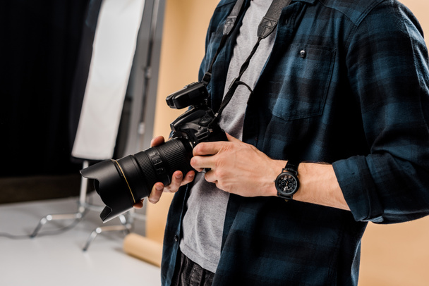 cropped shot of young photographer holding camera in photo studio - 写真・画像