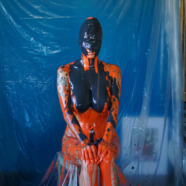 Young beautiful girl posing nude in studio doused with orange paint - Photo, Image