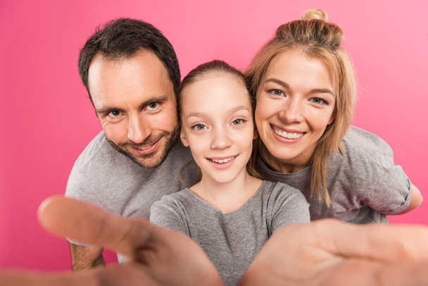 gelukkige dochter en lachende ouders tezamen selfie, geïsoleerd op roze - Foto, afbeelding