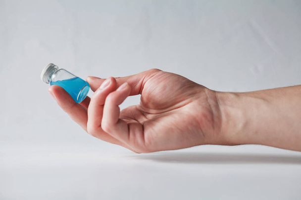 Human hand holding an old glass vial filled with cyan blue liquid on white blurred background - Zdjęcie, obraz