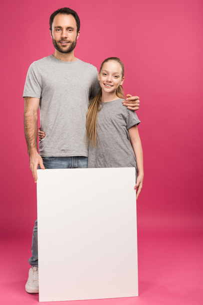 father hugging daughter and posing with blank placard, isolated on pink - Foto, Imagem