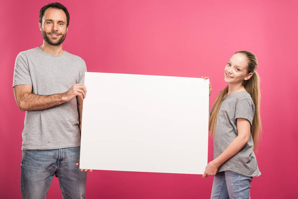 father and adorable daughter posing with empty board, isolated on pink - Фото, изображение