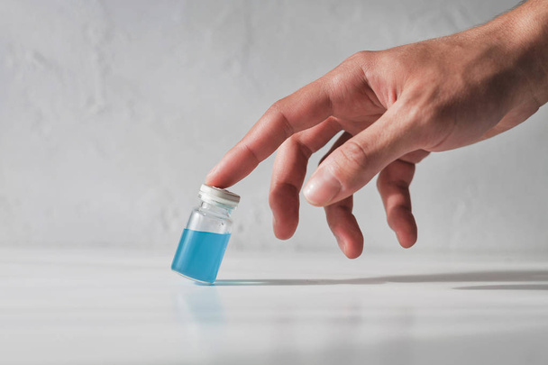 Human hand holding an old glass vial filled with cyan blue liquid on white blurred background - Fotografie, Obrázek