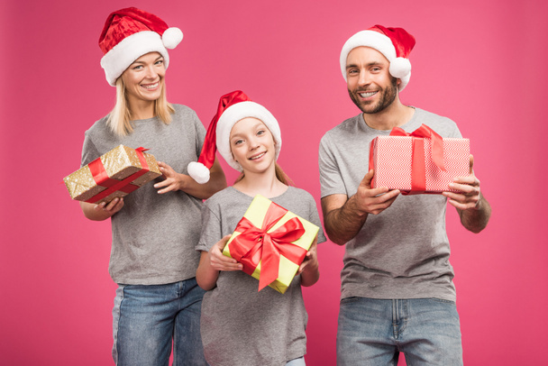 in santa hoeden houden van Kerstmis en gelukkige familie presenteert geïsoleerd op roze - Foto, afbeelding