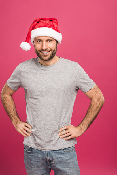 portrait of handsome smiling man in santa hat at christmastime, isolated on pink  - 写真・画像