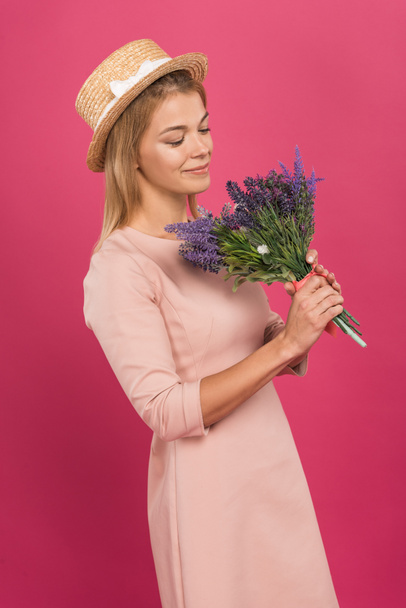 happy woman in straw hat looking at bouquet of flowers, isolated on pink - Valokuva, kuva
