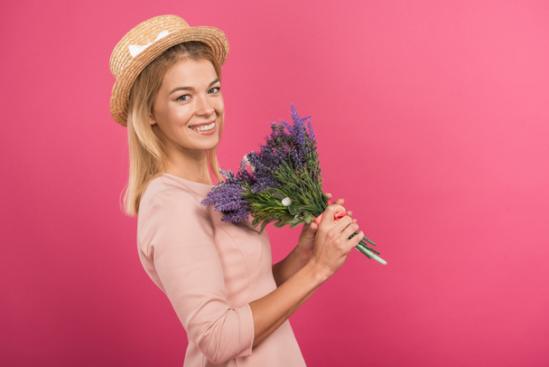 beautiful smiling woman posing in straw hat with flower bouquet, isolated on pink - Valokuva, kuva
