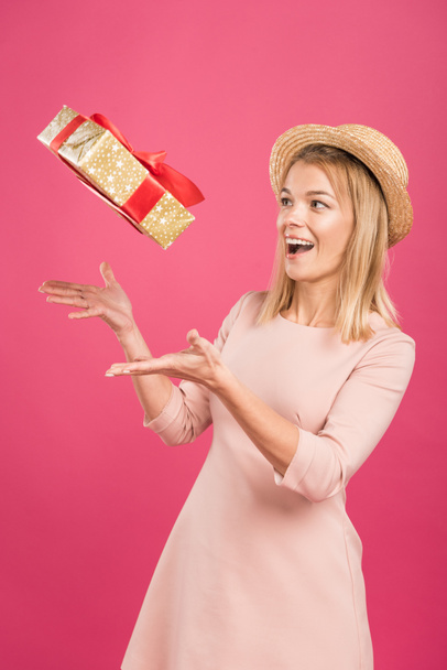 ενθουσιασμένος ξανθιά γυναίκα που ρίχνουν επάνω κουτί δώρου που απομονώνονται σε ροζ  - Φωτογραφία, εικόνα