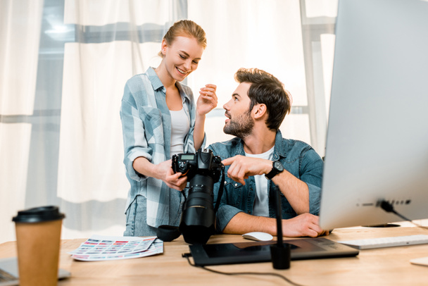professional young photographers using camera and smiling each other at workplace - Photo, Image