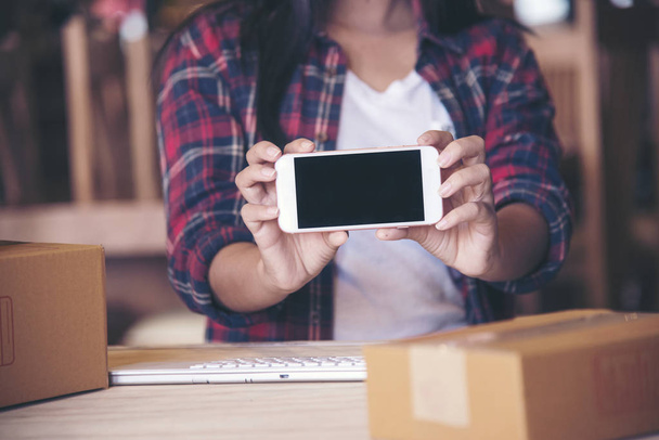 Beautiful woman holding phone,Young entrepreneur, teenager business owner work at home, box for delivery - Foto, immagini