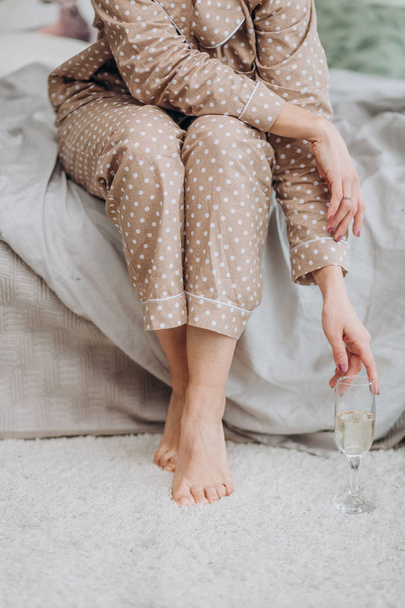 girl in a bedroom in beige pajamas with a glass of champagne nightdress - Zdjęcie, obraz