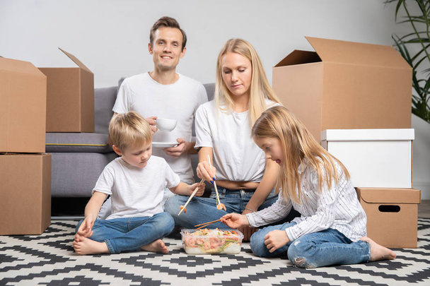 Picture of happy couple with children eating rice with shrimps sitting on floor - Photo, Image
