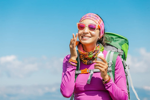 Πεζοπόρος γυναίκα εφαρμόζοντας αντηλιακή κρέμα για να προστατεύσει το δέρμα από την επικίνδυνη υπεριώδη ηλιακή ακτινοβολία ψηλά στα βουνά. Ταξίδια υγείας έννοια - Φωτογραφία, εικόνα