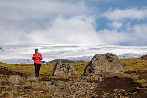 A young woman with a backpack travels around Iceland. Front view of a tourist walking through a mountainous area on a sunny day. - Foto, Bild