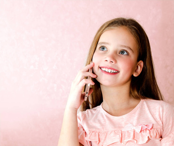 Portrait of cute smiling  little girl calling by cell phone smartphone  isolated on pink background - Φωτογραφία, εικόνα