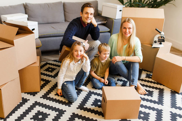 Photo of parents with children sitting on floor among cardboard boxes t - Foto, imagen