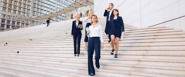 Foreign managers in official journey speaking on stairs with tablet and document cases. Concept of business trip and waiting for conference. Confident people talking in suits and white shirts. - Photo, Image