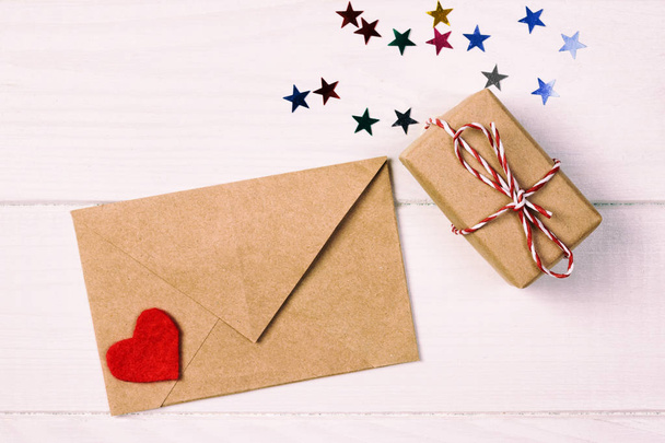 Φάκελος αλληλογραφίας με κόκκινη καρδιά και δώρο κουτί πάνω από λευκό τονισμένο, vintage ξύλινο υπόβαθρο. Κάρτα ημέρα του Αγίου Βαλεντίνου, αγάπη ή γάμο χαιρετισμό έννοια. - Φωτογραφία, εικόνα