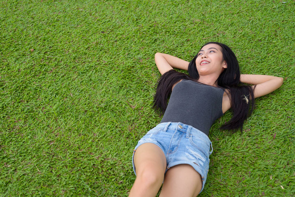 Happy young beautiful Asian woman laying down on grass at the park - Фото, зображення