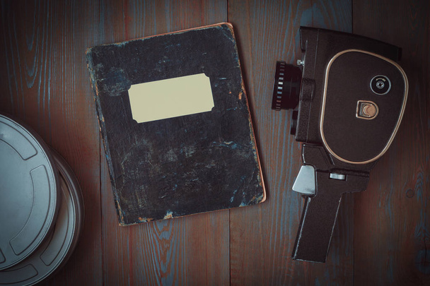 Стара кінокамера, коробка фільмів і блокнот для нотаток лежать на столі
 - Фото, зображення
