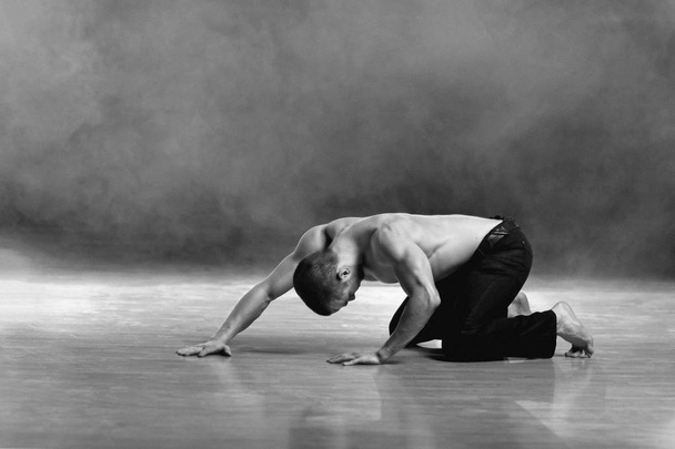 junger, muskulöser Mann in zeitgenössischer Tanzpose auf einer Bühne. - Foto, Bild