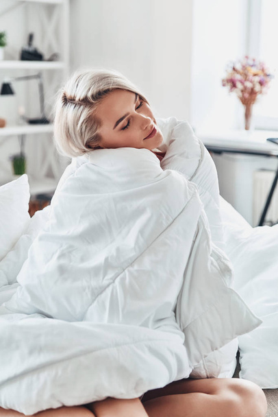 Jovem atraente olhando para longe enquanto cobria com cobertor na cama em casa
 - Foto, Imagem