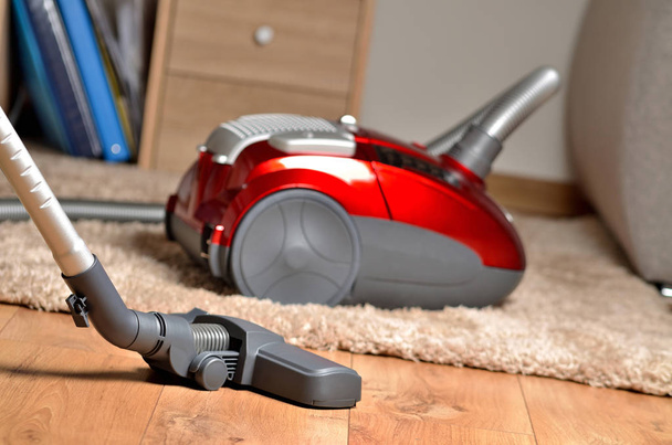 Vacuum cleaner on floating floor and shaggy carpet, desk with files and sofa in background - Photo, Image