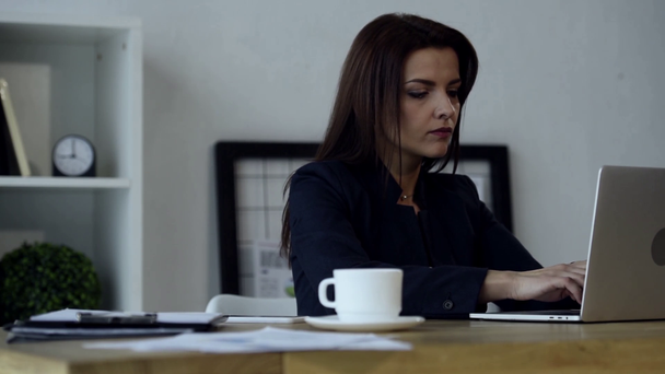 focused businesswoman typing on laptop at table with coffee cup in modern office  - Footage, Video