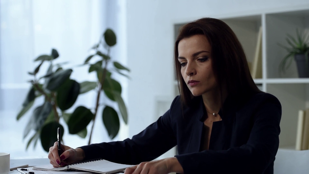 mujer de negocios adulta seria escribiendo en libro de texto en la mesa en la oficina
  - Metraje, vídeo