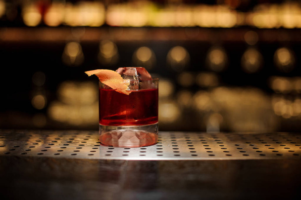Glass of a Boulevardier cocktail with orange zest and ice cube on the steel wooden bar counter - Photo, image
