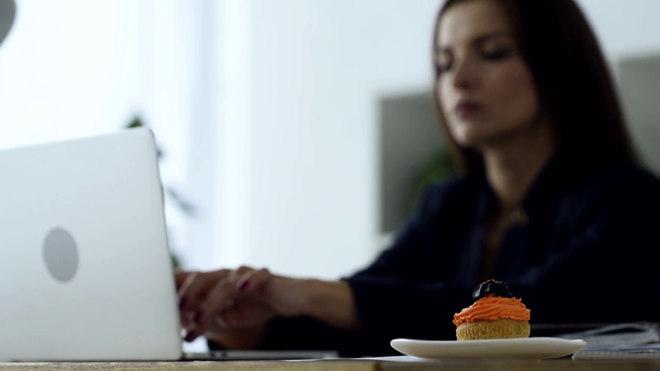 selective focus of delicious cupcake on table and businesswoman working behind in office  - Footage, Video