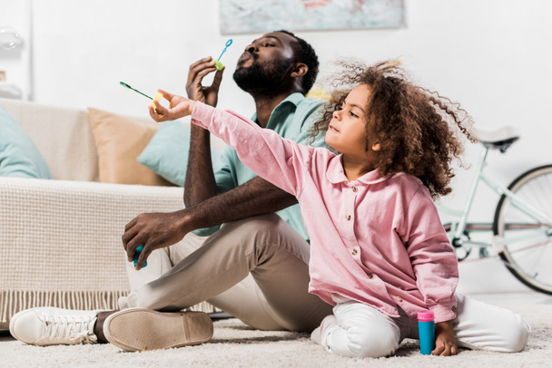 african american family blowing soap bubbles in living room  - Фото, зображення