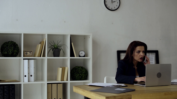 агрессивная деловая женщина жестикулирует вручную, разговаривая на смартфоне, эмоционально закрывая ноутбук и бросая бумагу со стола в офисе
  - Кадры, видео