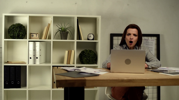 Взрослая раздраженная деловая женщина, печатающая на ноутбуке и сидящая с руками на голове за столом в офисе
  - Кадры, видео