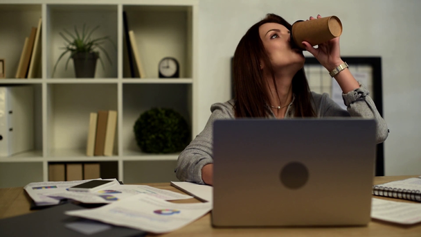 foyer sélectif de femme d'affaires fatiguée écrivant dans le manuel et buvant du café à table avec ordinateur portable dans le bureau
  - Séquence, vidéo