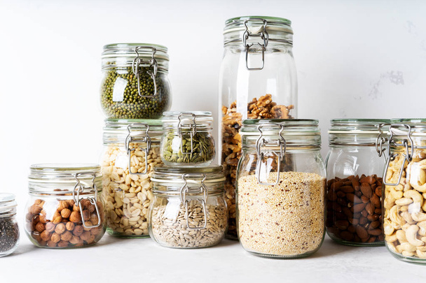 Glass jars with various nuts, beans and seeds on light background - Photo, image