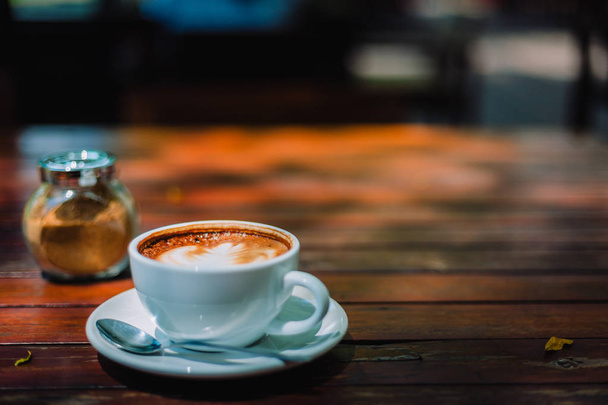 Hete koffie latte cappuccino spiraal schuim op houten tafel in koffiehuis café met vintage Toon filter achtergrondkleur. Met kopie ruimte voor uw tekst. Toon kleureffect - Foto, afbeelding