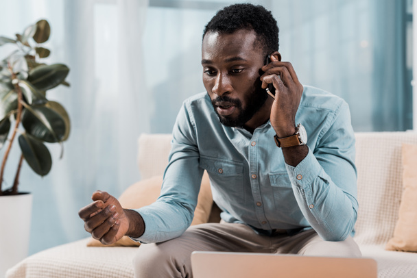 worried african american man talking on smartphone at home - Photo, Image