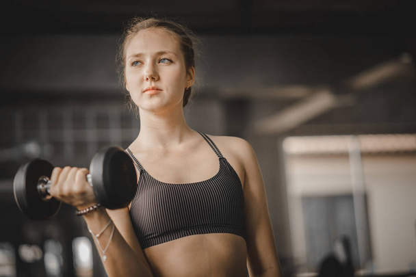 Fit beautiful young woman caucasian posing at the camera in sportswear. Young woman holding dumbbell during an exercise class in a gym. Healthy sports lifestyle, Fitness concept. - Φωτογραφία, εικόνα