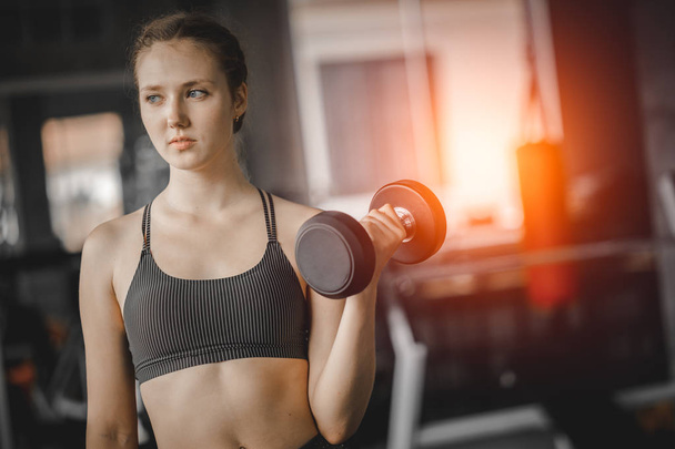 Fit beautiful young woman caucasian posing at the camera in sportswear. Young woman holding dumbbell during an exercise class in a gym. Healthy sports lifestyle, Fitness concept. - Photo, Image