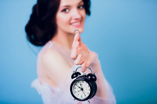 Beautiful charming girl in white wedding dress, being late in morning, and holding in her hand retro alarm clock and ring - Foto, imagen