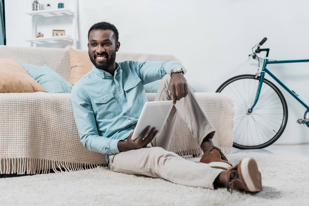 Američan Afričana muž sedí na podlaze a používání digitálních tabletu v obývacím pokoji - Fotografie, Obrázek