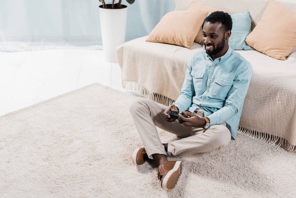 african american man sitting on floor and playing video game in living room - Φωτογραφία, εικόνα