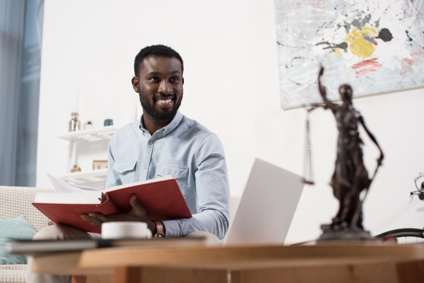 Afrikanisch-amerikanischer Mann hält Buch in den Händen und schaut im Wohnzimmer weg - Foto, Bild