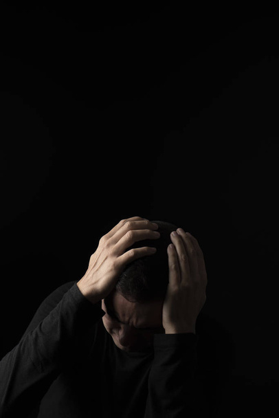 closeup of a desperate young caucasian man with his hands in his head, against a black background, with some blank copy space around him - Photo, Image