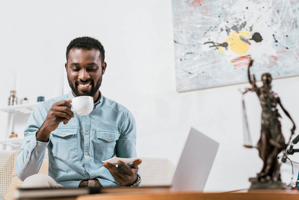 african american man drinking coffee from cup in living room - Foto, afbeelding