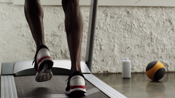 vista parcial del deportista afroamericano corriendo en cinta de correr en el gimnasio en cámara lenta
 - Metraje, vídeo