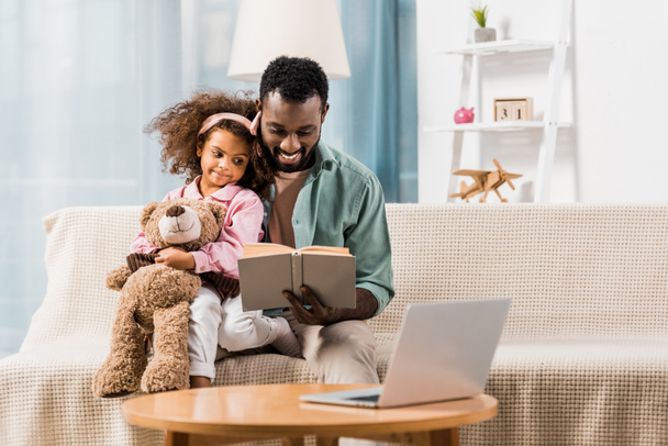 african american man reading with daughter in living room - Photo, Image
